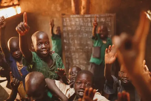 Young students in Kitgum, Uganda, enthusiastically participate in class, raising their hands with smiles.